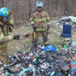 Firefighters Mike Rayburn and Kyle Corey use a portable tank and hand tools to extinguish a trash fire