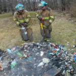 Firefighters Mike Rayburn and Kyle Corey use a water can to extinguish a backyard trash fire